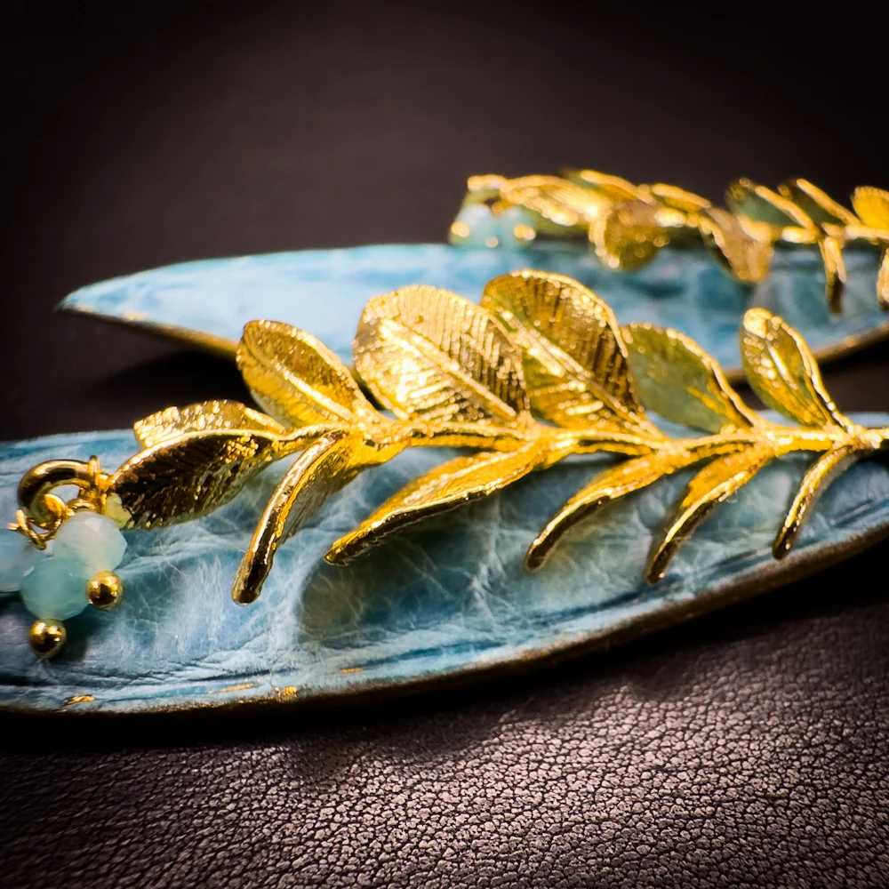 Détail du rameau végétal doré à l'or fin 24 carats, des perles d'amazonite céladon et du cuir d'alligator bleu